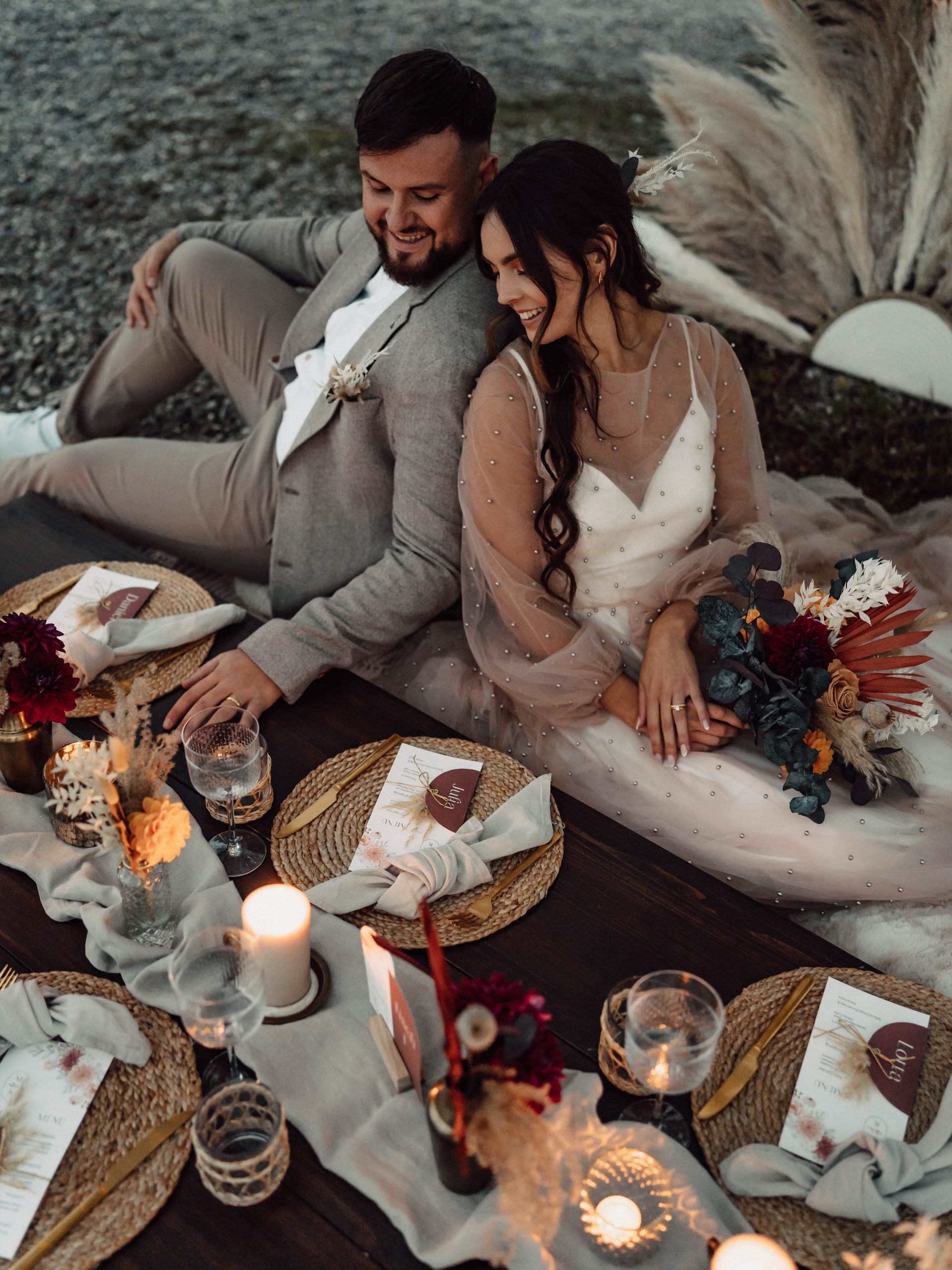 Ein Brautpaar sitzt am dekorierten Hochzeitstisch. Die Braut hält den Brautstrauß in der Hand.